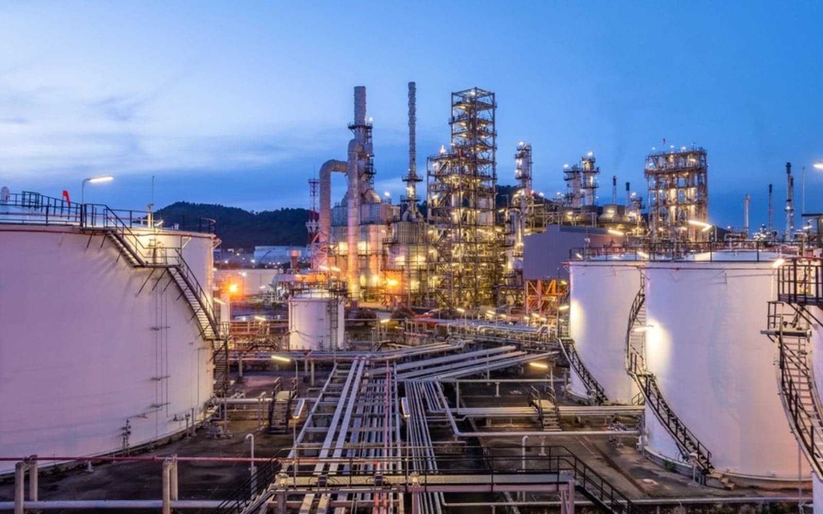 Oil and gas process plant with storage tanks and pipe racks at dusk