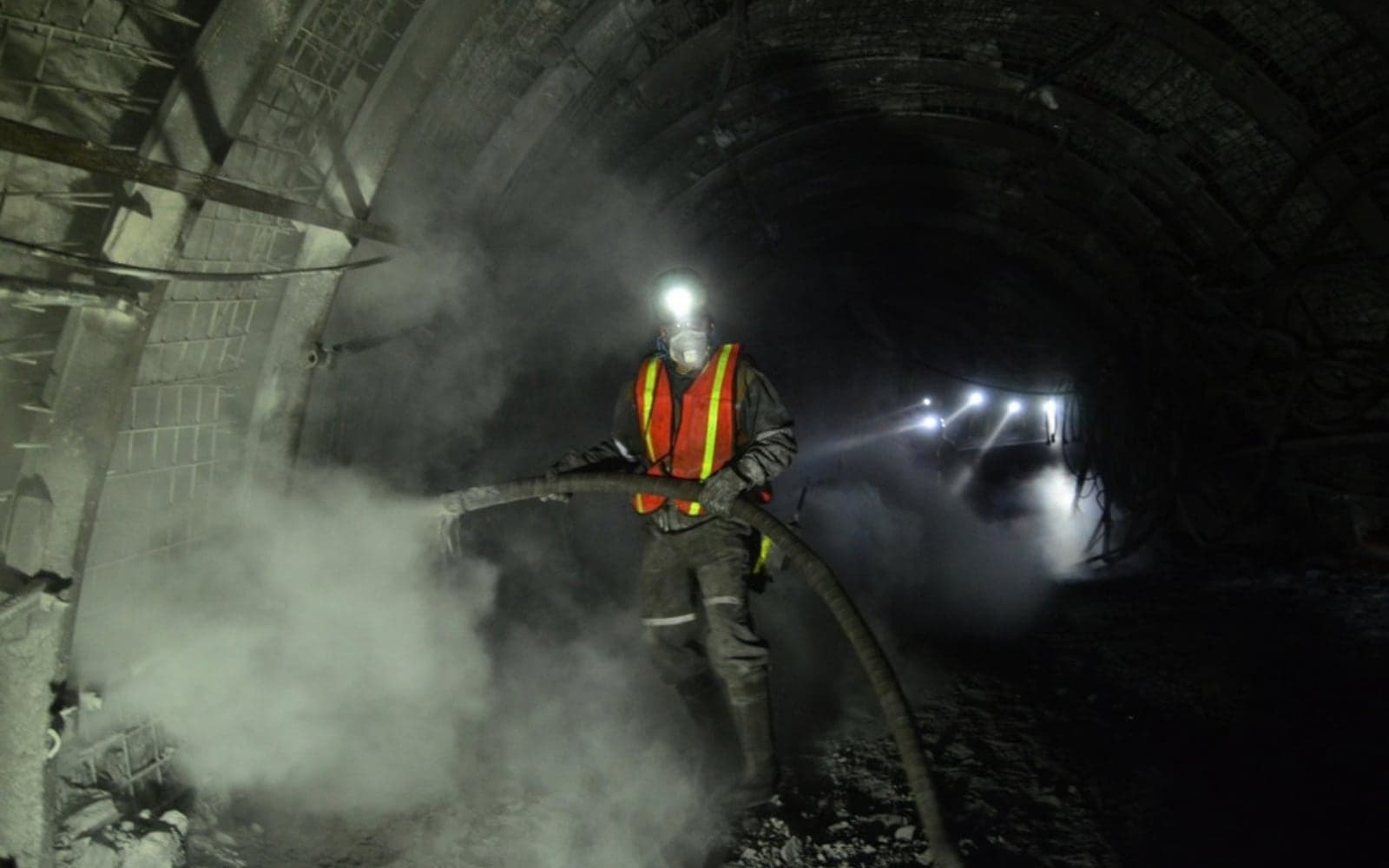 Miner in a helmet and high-visibility vest working in an underground mine tunnel